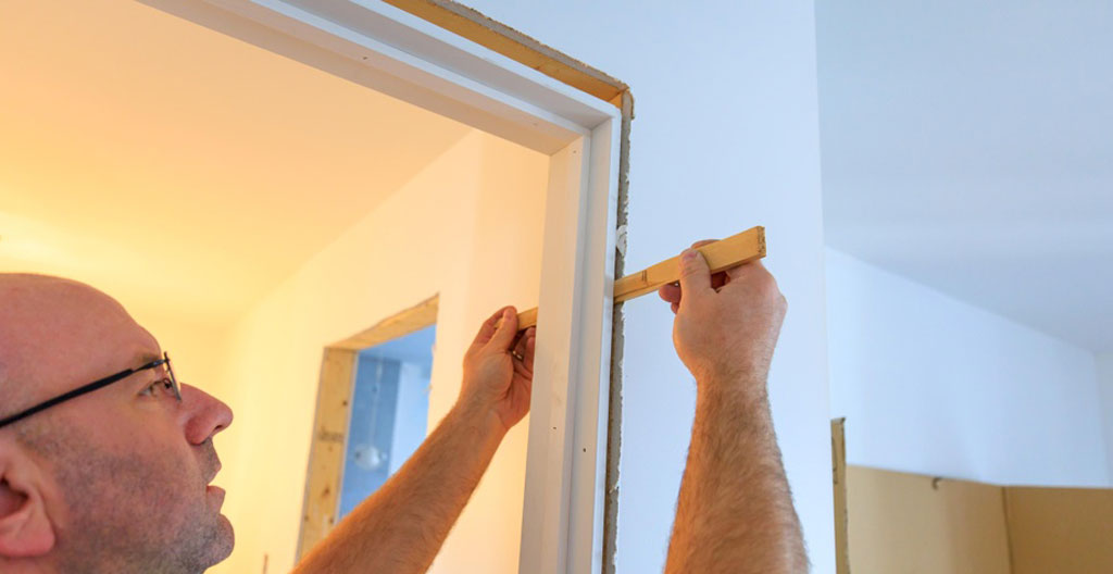 Installateur professionnel inspectant jonction cadre porte avec outil de mesure dans entrée maison québécoise