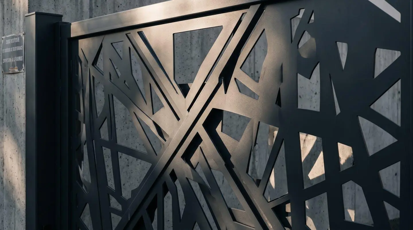 Détail portillon aluminium anthracite avec découpe laser personnalisée en motif géométrique contemporain, lumière rasante accentuant relief