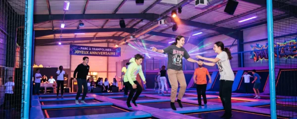 Teenagers jumping on trampolines during a nighttime session in an indoor trampoline park with UV and neon lighting.