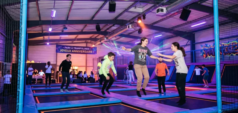 Teenagers jumping on trampolines during a nighttime session in an indoor trampoline park with UV and neon lighting.