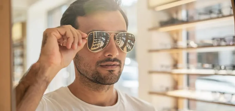 Un homme essaie des lunettes aviateur devant un miroir en opticien.